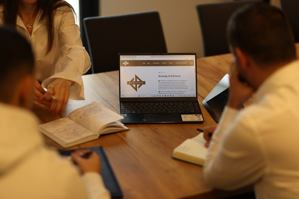 Team meeting with laptop showing the Kostrateg website and Strategy &amp; Advisory